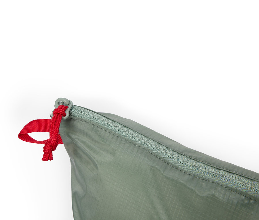 Gros plan d'un sac vert olive avec fermeture éclair et cordon de serrage rouge sur fond blanc.