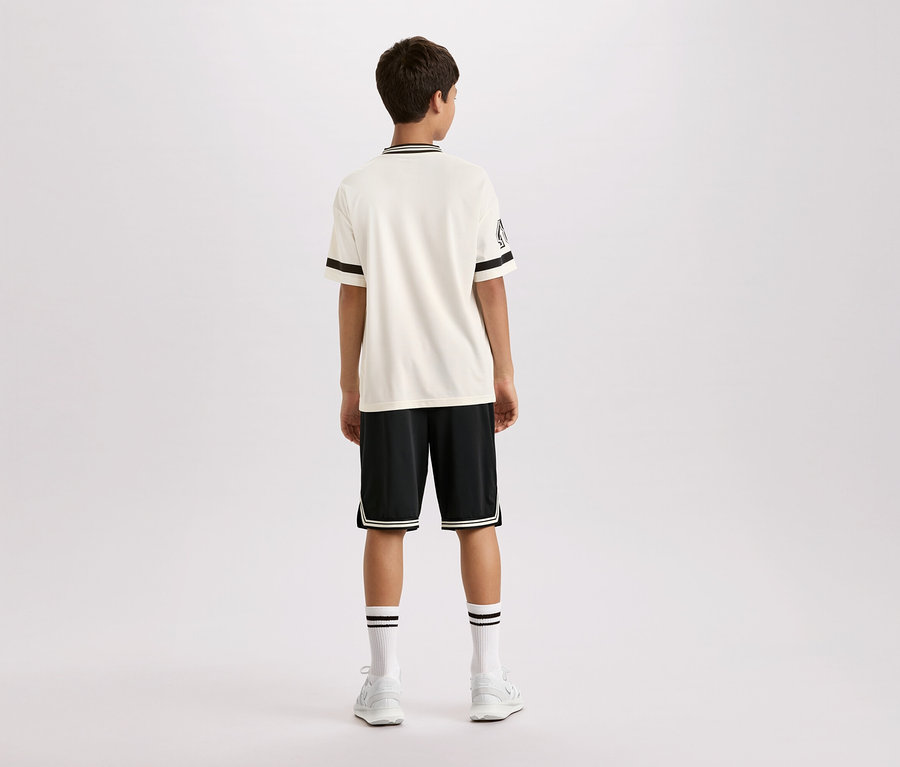 Vue arrière d'un jeune homme portant une chemise crème à manches courtes avec des rayures noires au col et aux manches, un short noir avec des rayures blanches et des chaussettes et chaussures blanches.
