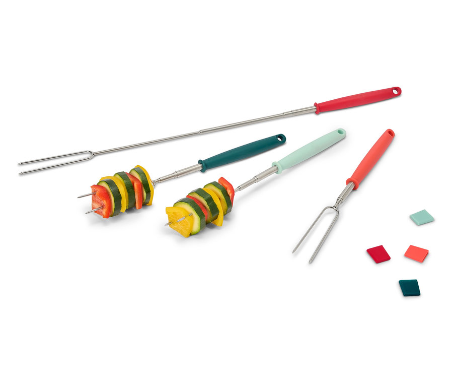 Quatre brochettes de barbecue, dont deux avec des légumes, sont posées sur un fond blanc. Les brochettes ont des manches rouges, verts et orange.