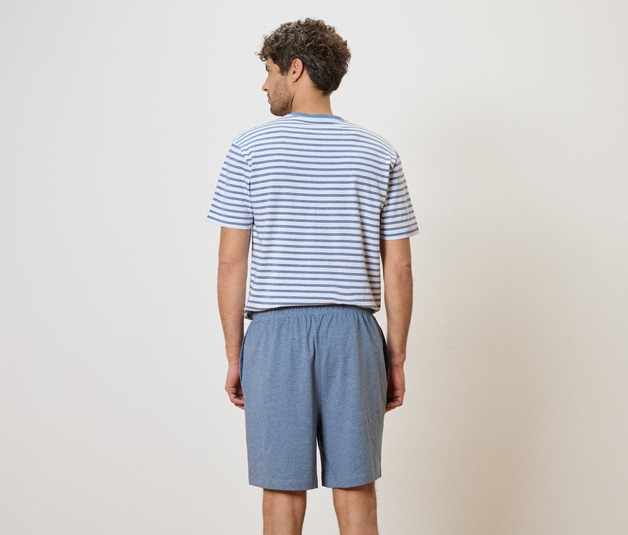 Vue arrière d'un homme aux cheveux bouclés portant un t-shirt rayé bleu et blanc et un short bleu sur un fond crème.
