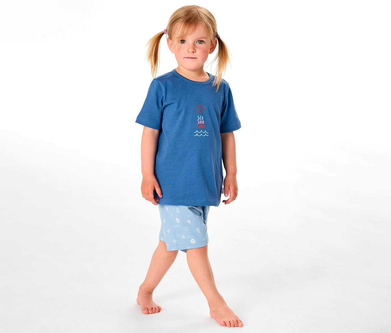 Une fille porte un pyjama court pour enfant SCHIESSER, composé d'un haut bleu et d'un short bleu clair à motifs.