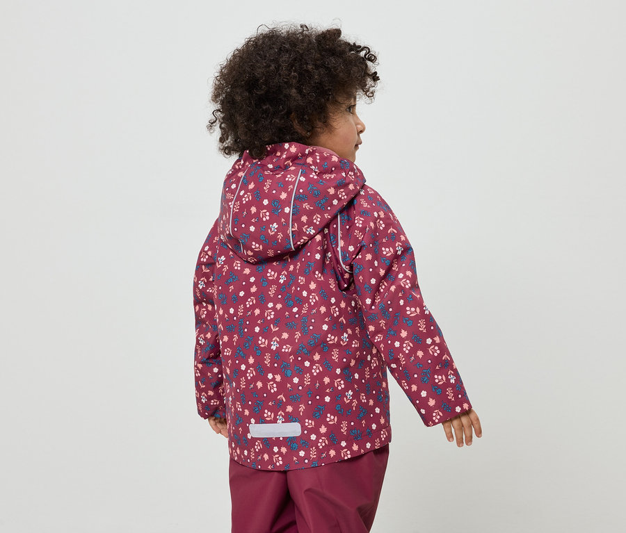 Un enfant aux cheveux bouclés, vu de dos, porte une veste bordeaux à motifs floraux et un pantalon assorti.
