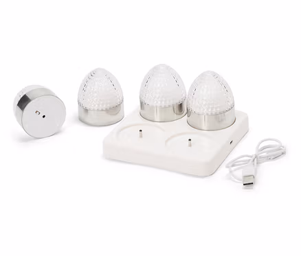Quatre petites lampes rondes avec des bases argentées et des coupoles en verre transparent à facettes sont posées sur une station de charge blanche avec un câble USB.