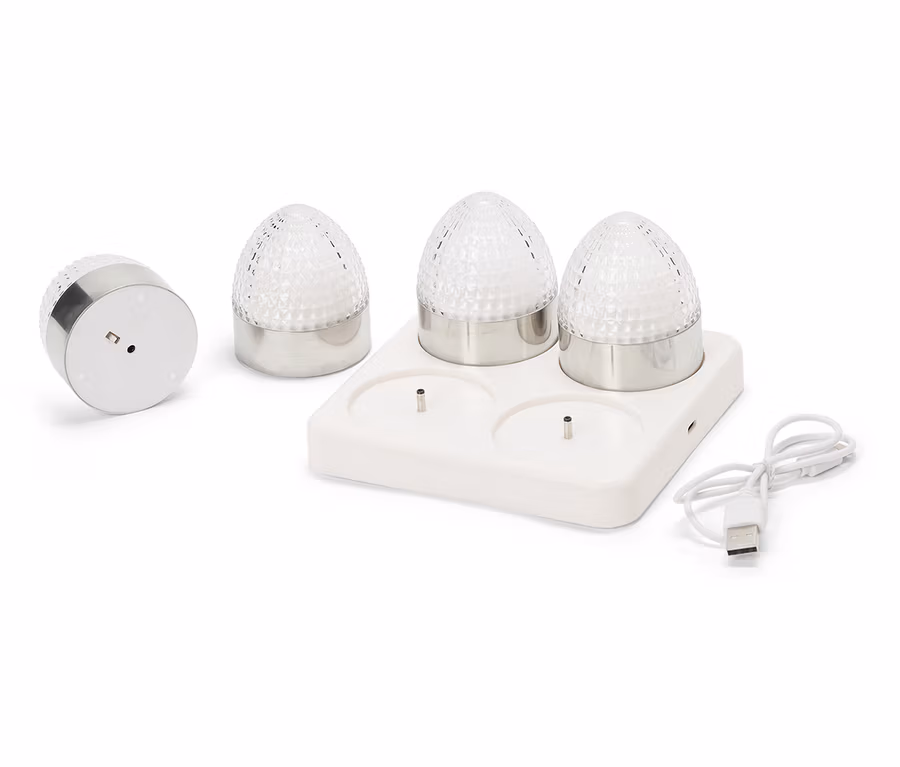Quatre petites lampes rondes avec des bases argentées et des coupoles en verre transparent à facettes sont posées sur une station de charge blanche avec un câble USB.