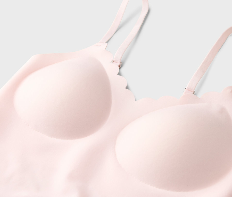 Gros plan d'un soutien-gorge rose clair à fines bretelles et décolleté ondulé sur fond neutre.
