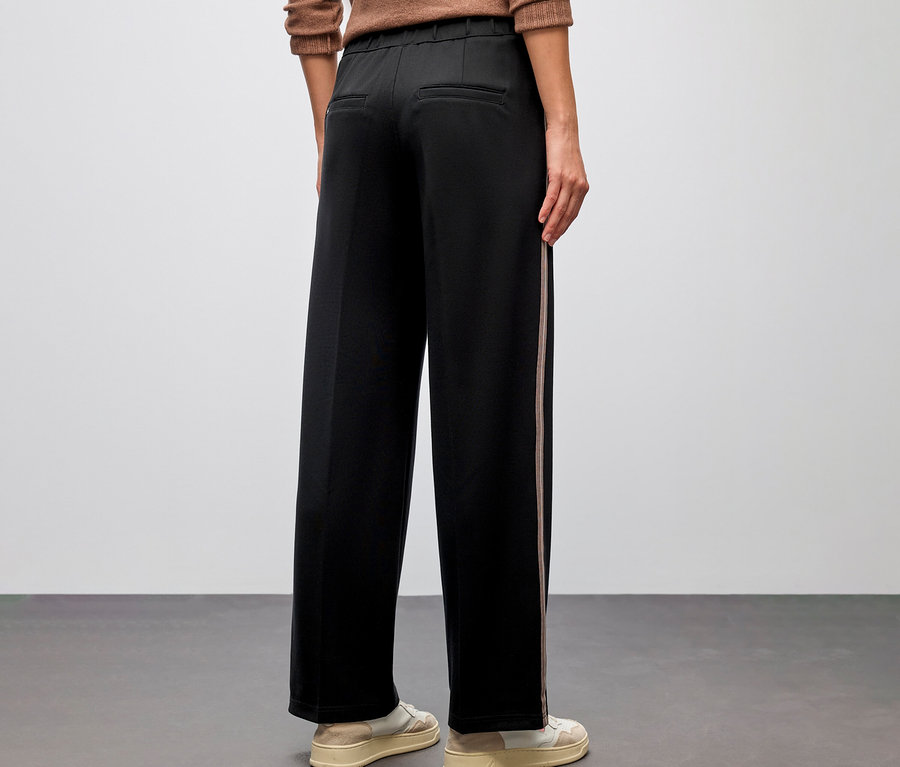 Personne vue de dos portant un chemisier marron et un pantalon droit noir avec galon Street One et des baskets crème.