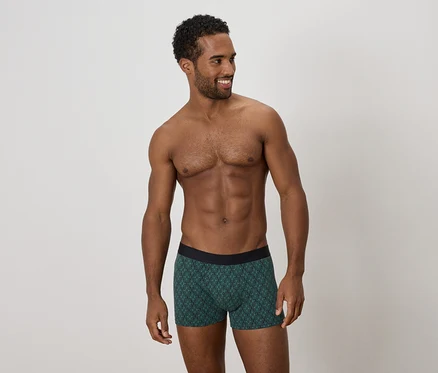 Homme torse nu portant un boxer vert à motifs regardant sur le côté.