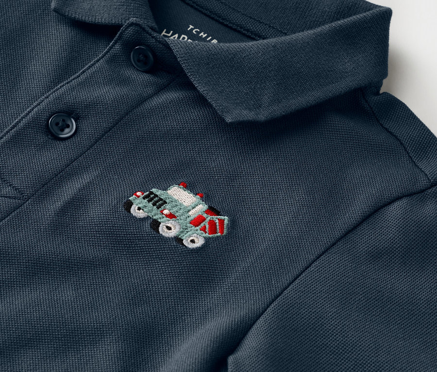 Gros plan d'un polo bleu marine avec une petite illustration brodée d'une jeep verte avec des accents rouges.