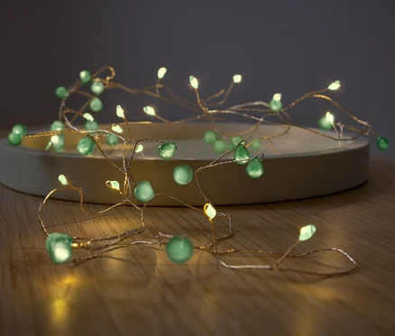 Guirlande lumineuse avec des pierres décoratives vertes sur une assiette beige.