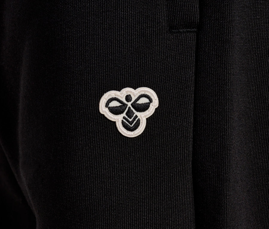 Gros plan sur un pantalon noir avec un petit logo Hummel blanc.