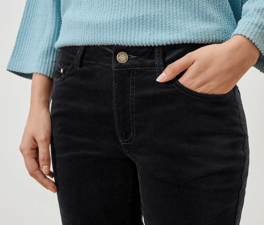 Gros plan d'une personne avec une main dans la poche d'un pantalon noir et un haut bleu.