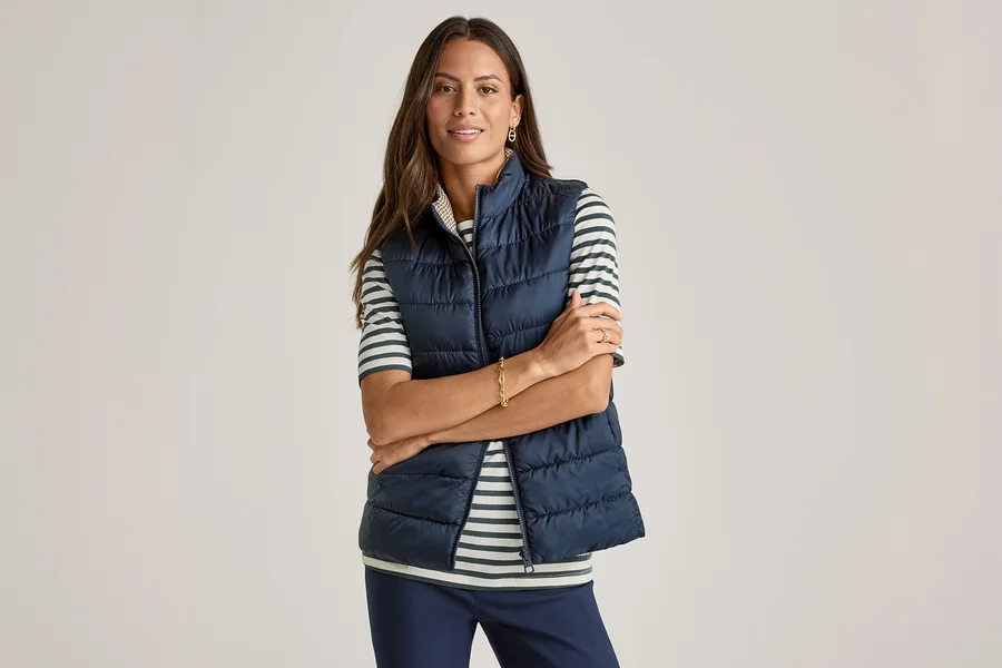 Une femme les bras croisés porte un gilet bleu marine sur un T-shirt demi-manches, vert à rayures.