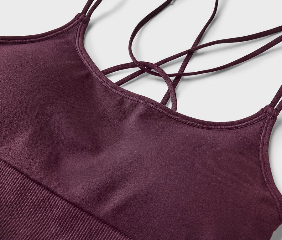 Gros plan d'un soutien-gorge de sport marron châtaigne avec de fines bretelles croisées sur un fond gris clair.