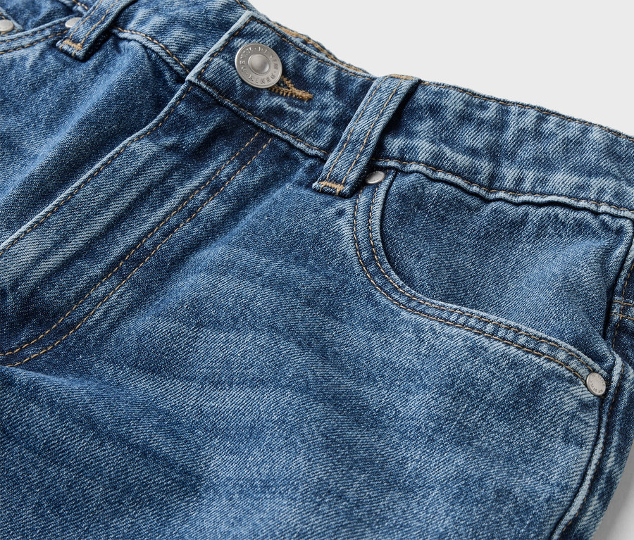 Gros plan d'un jean bleu avec bouton, passant de ceinture et poche sur fond blanc.