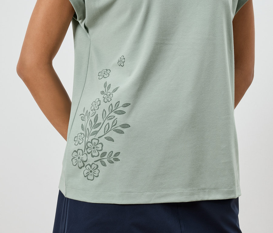 Gros plan d'une femme portant un t-shirt vert clair à motif floral et un pantalon bleu marine.
