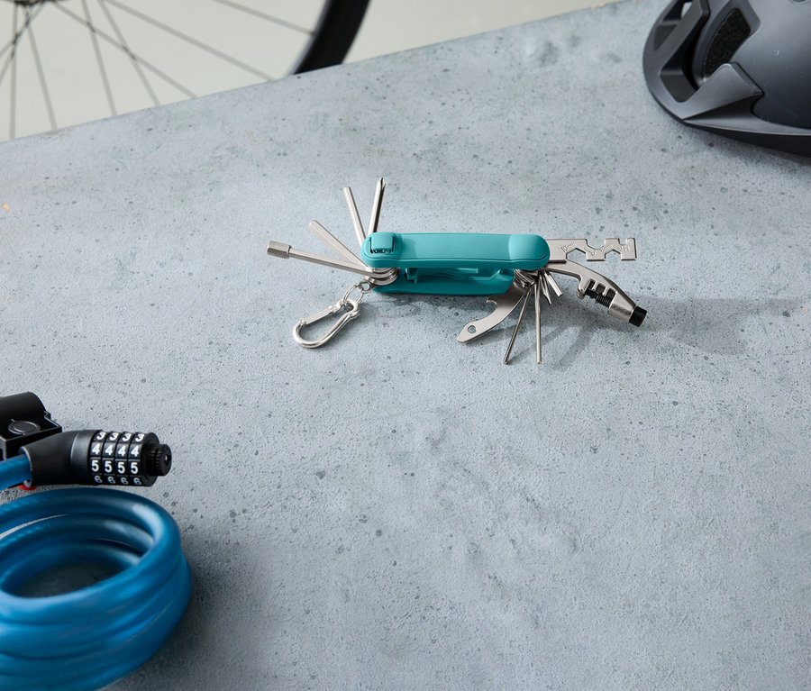 Sur une surface grise se trouvent un multi-outil turquoise, un cadenas à câble bleu et un casque de vélo gris.