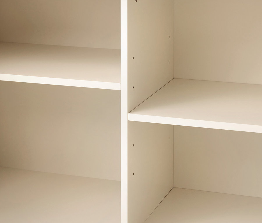 Gros plan d'étagères vides de couleur beige clair, montrant deux sections verticales avec plusieurs compartiments horizontaux et de petits trous de réglage.