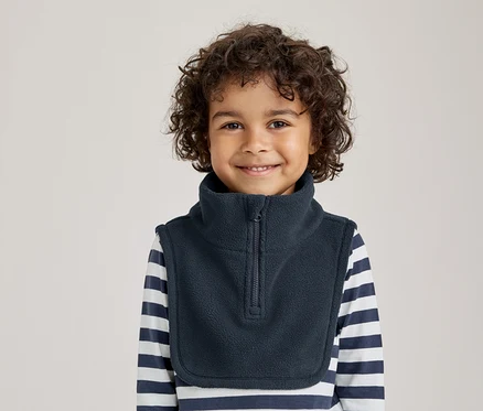 Jeune enfant aux cheveux bouclés souriant, portant un cache-cou en polaire bleu foncé sur un t-shirt à manches longues rayé.