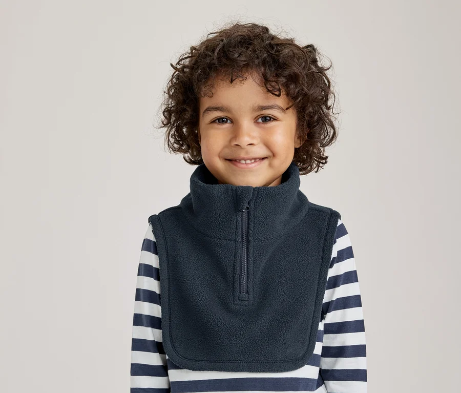 Jeune enfant aux cheveux bouclés souriant, portant un cache-cou en polaire bleu foncé sur un t-shirt à manches longues rayé.