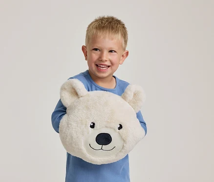 Un petit garçon souriant vêtu d'un haut bleu tient un oreiller ours blanc et moelleux.