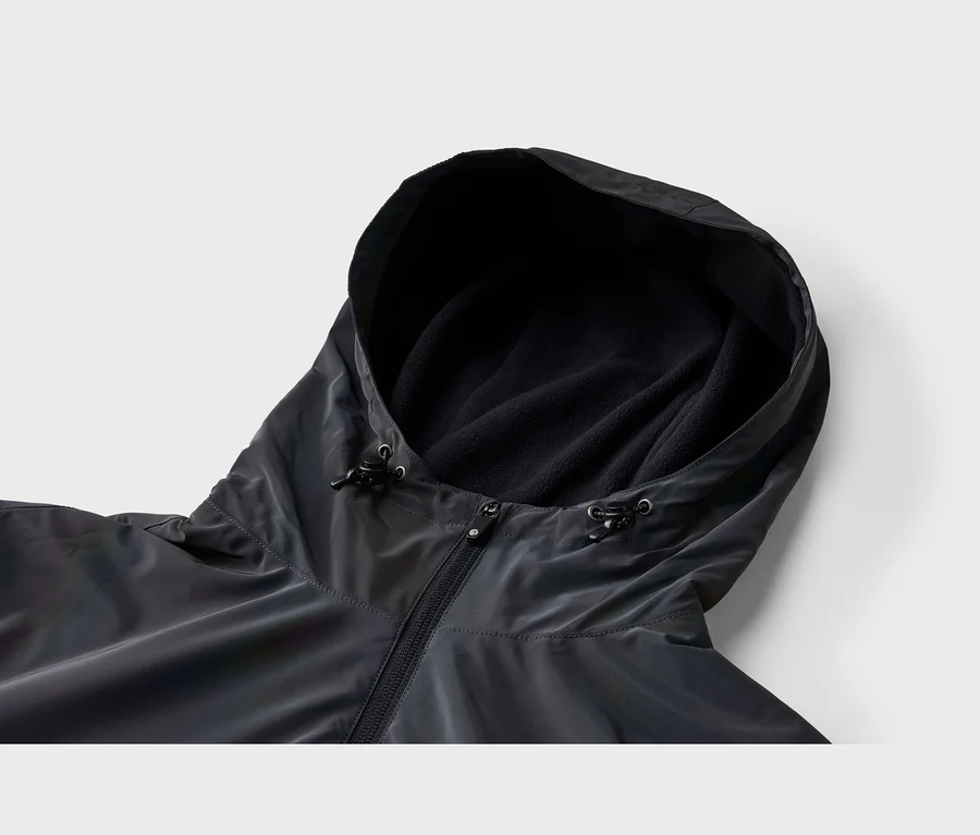 Gros plan d'une veste sombre, potentiellement irisée, avec une capuche. La capuche est doublée de polaire noire et possède des cordons de serrage réglables. Une fermeture éclair noire est visible sur le devant.