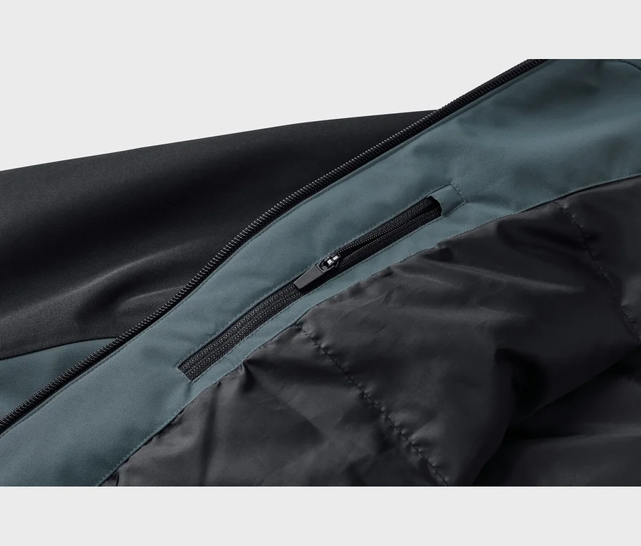 Gros plan d'une veste noire et bleu sarcelle foncé, montrant une fermeture éclair noire avec une tirette et une petite poche zippée cachée sur le panneau bleu sarcelle foncé, à côté d'une doublure noire matelassée.