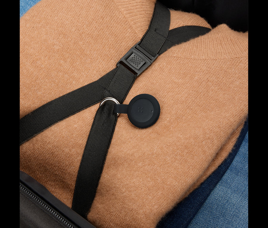 Un pull marron et un jean bleu sont placés dans une valise, avec une sangle noire et un pendentif rond noir par-dessus.
