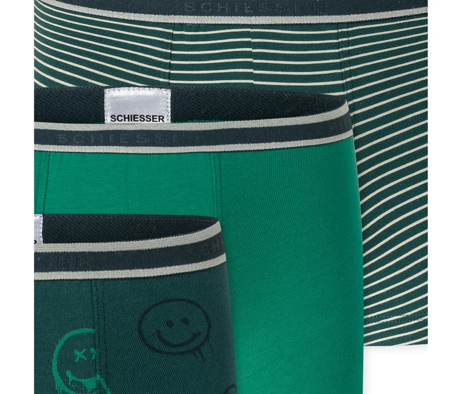 Trois shorts pour enfants SCHIESSER : un vert foncé à rayures blanches, un vert clair uni et un vert foncé à motifs de smileys noirs.