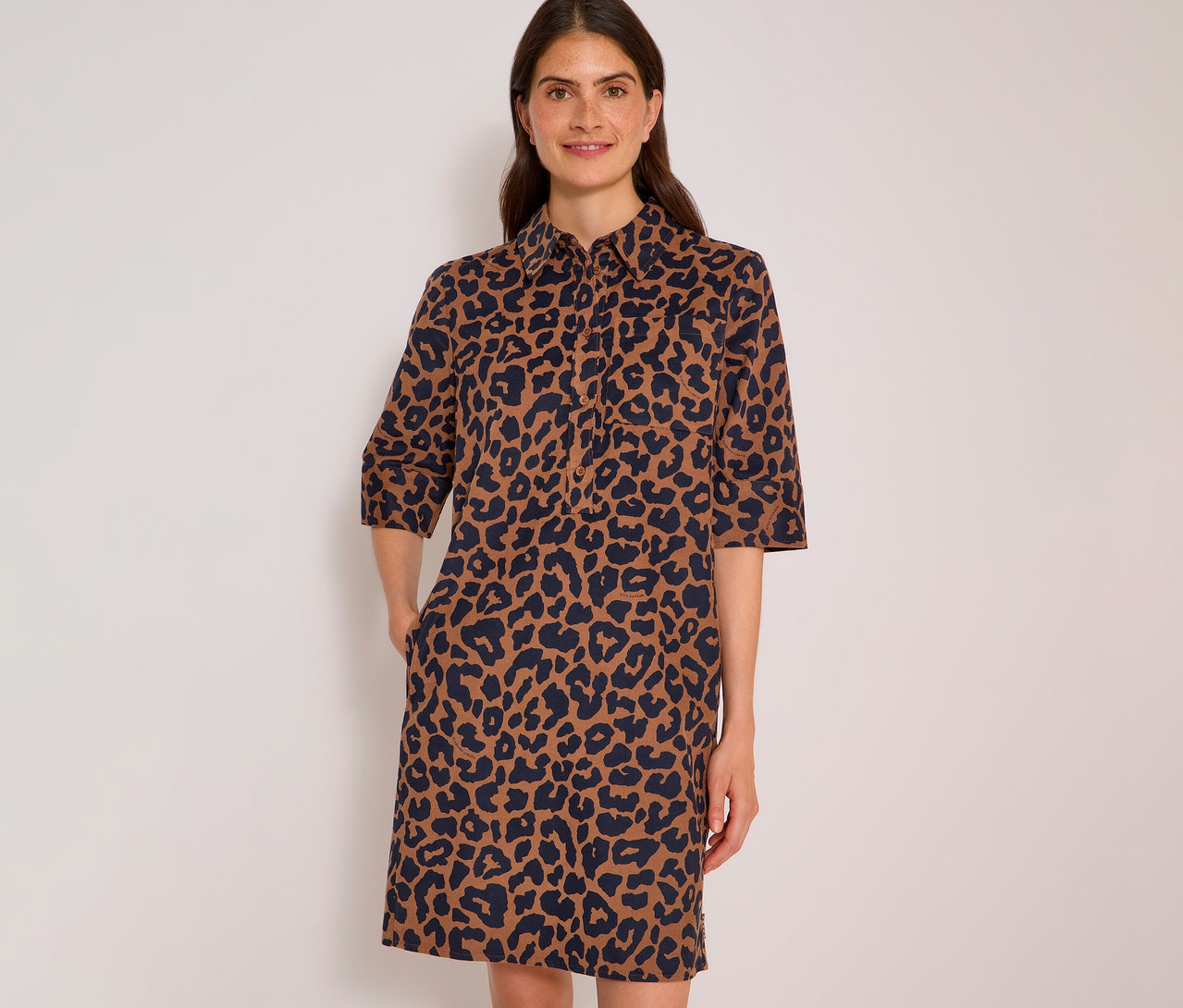 Femme souriante portant une robe chemise CECIL à imprimé léopard marron et bleu foncé, manches 3/4, mains dans les poches.