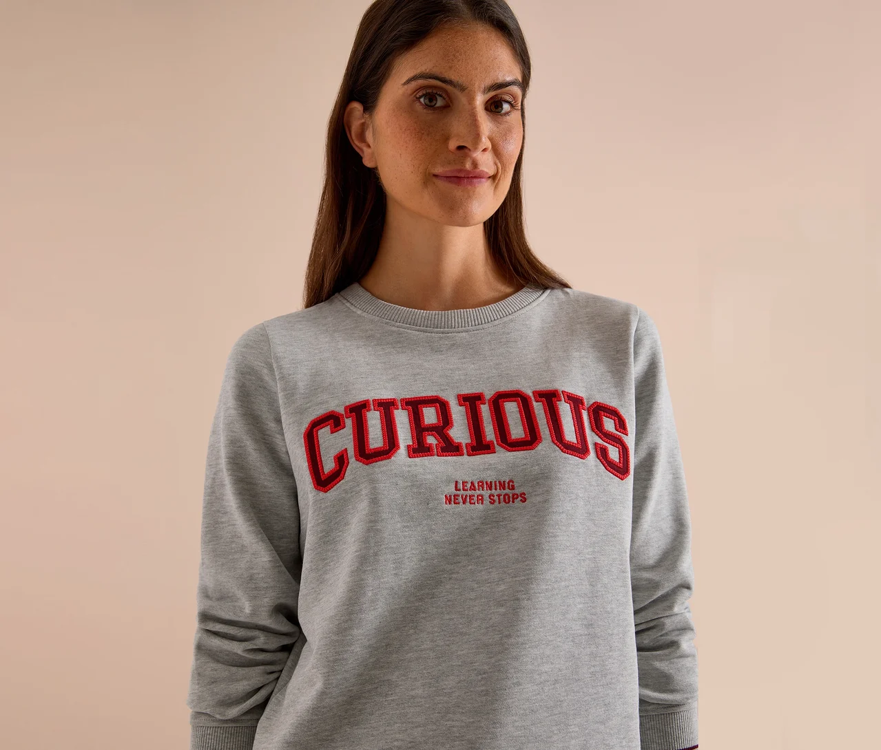 Femme portant un sweatshirt CECIL gris avec l'inscription rouge "CURIOUS" et "LEARNING NEVER STOPS".