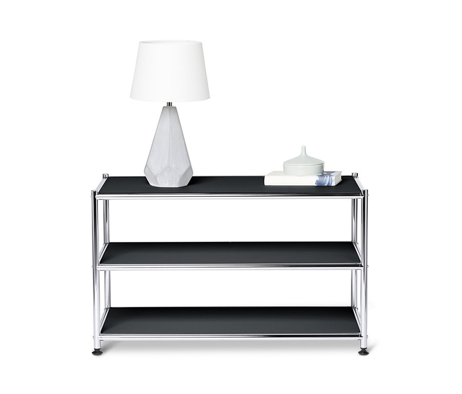 Sur l'étagère supérieure de la table basse en métal « CN3 », ouvert, noir, se trouvent une lampe et des décorations.