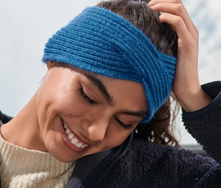 Femme souriant et touchant ses cheveux, portant un bandeau en maille bleu.