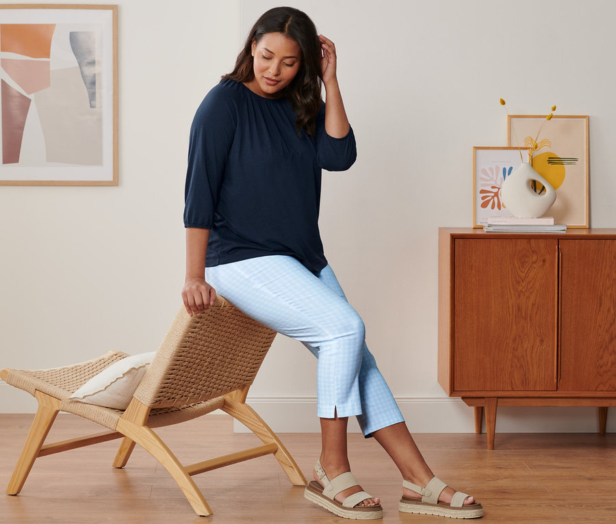 Une femme est assise sur une chaise et porte un t-shirt à manches 3/4 bleu foncé, un pantalon stretch 7/8 bleu clair et blanc et des sandales à plateforme en cuir.