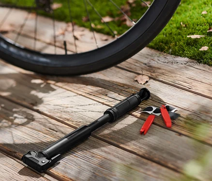Un vélo noir est posé sur un plancher en bois à côté d'une mini-pompe à vélo et d'un kit de réparation.