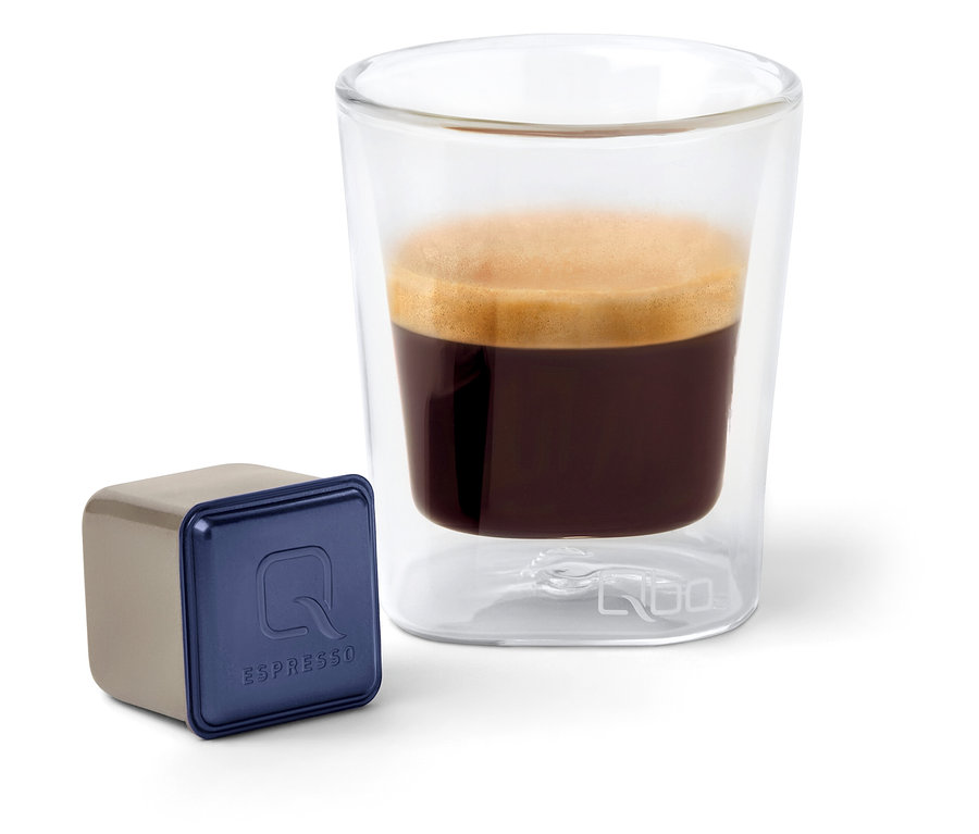 Une capsule de café Qbo Espresso INDIAN KAVERI à côté d'un verre d'espresso.