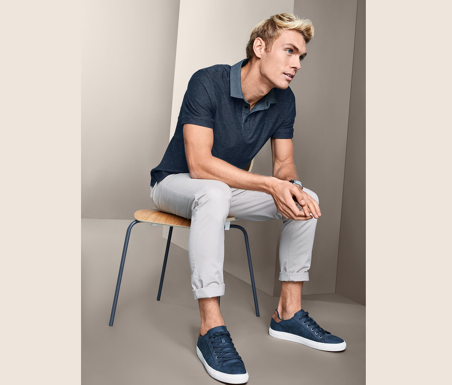 Un homme est assis sur une chaise et porte un polo en jacquard, un pantalon et des baskets.