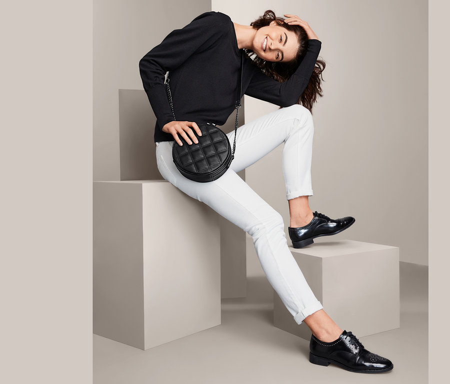 Femme assise sur des cubes posant avec un sac à bandoulière rond.