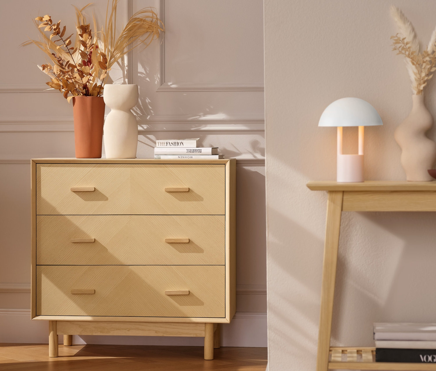 Une commode à tiroirs en frêne avec des façades décoratives à côté d'un fauteuil gris avec une couverture orange.