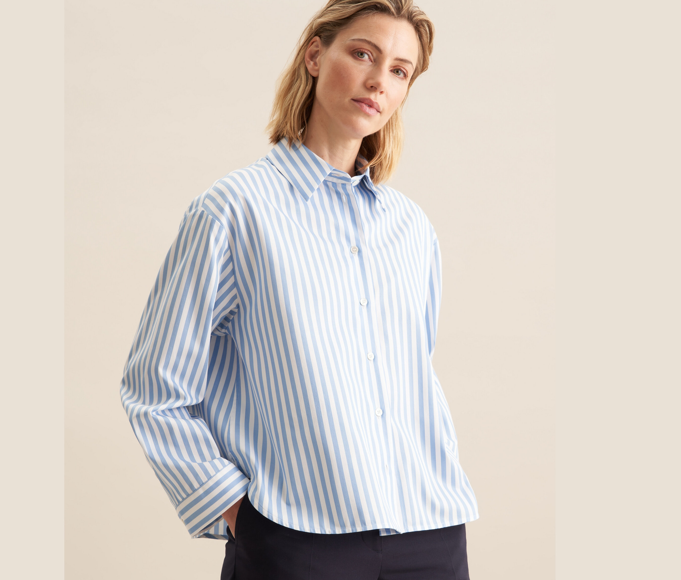 Une femme porte une chemise oversize bleue à rayures blanches Seidensticker et un pantalon bleu foncé.
