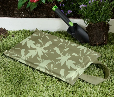 Un coussin pour genoux est posé sur l'herbe à côté d'une pelle et d'une plante.