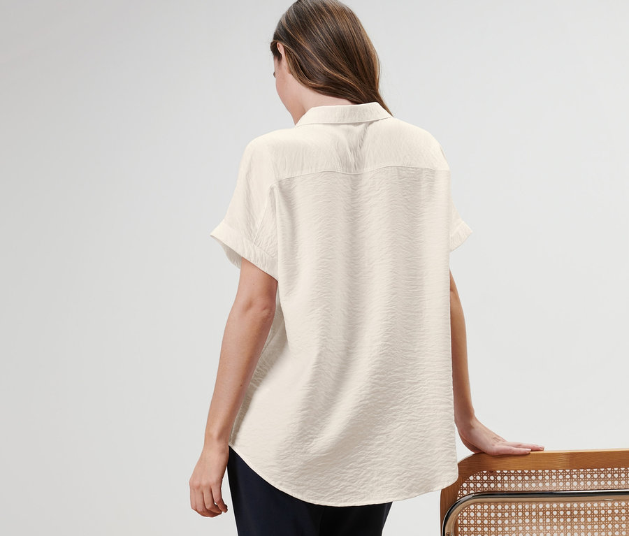 Une femme, vue de dos, porte une blouse et s'appuie sur une chaise.