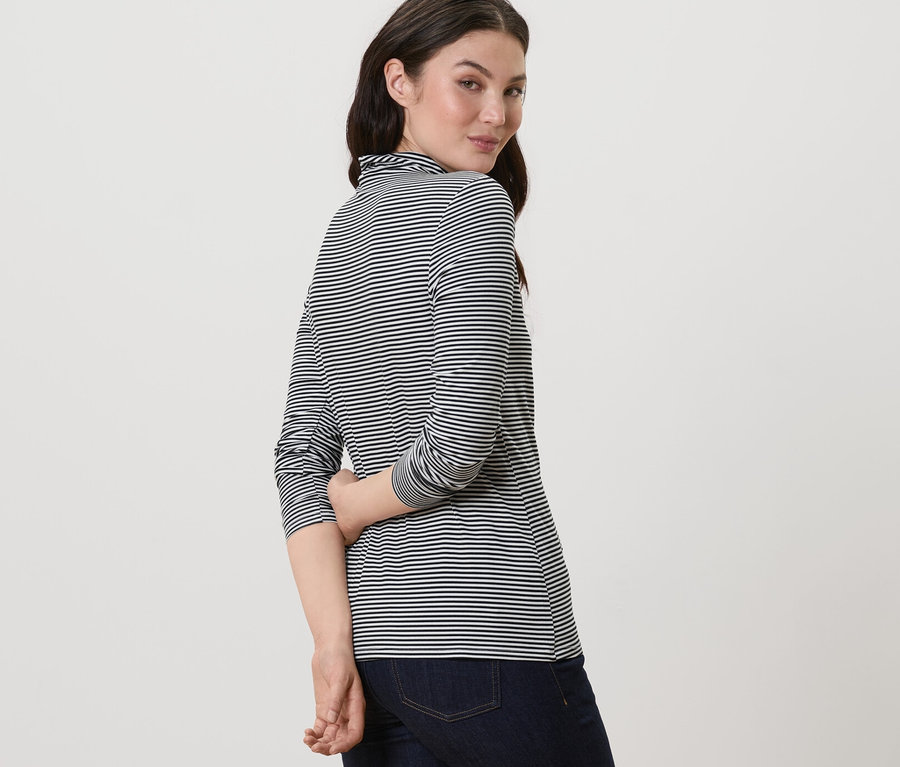 Femme regardant par-dessus son épaule portant une blouse rayée à col montant et un jean.