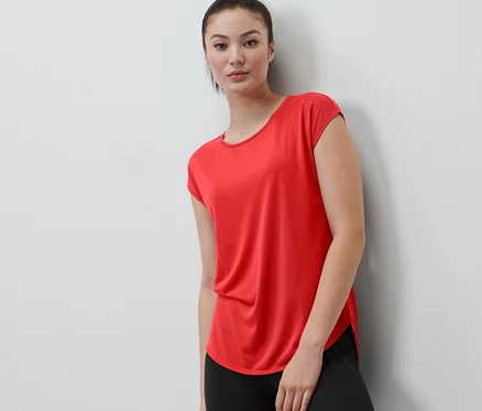 Une femme appuyée contre un mur porte un t-shirt de sport rouge.