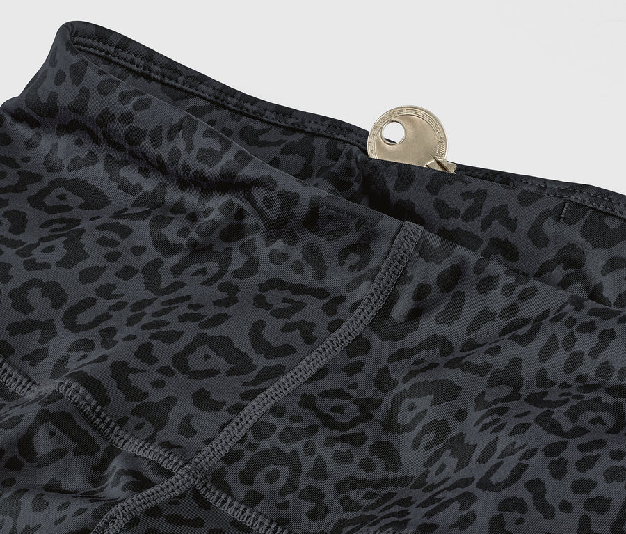 Vue détaillée d'un legging de sport gris et noir avec un motif léopard et une clé dans la poche.