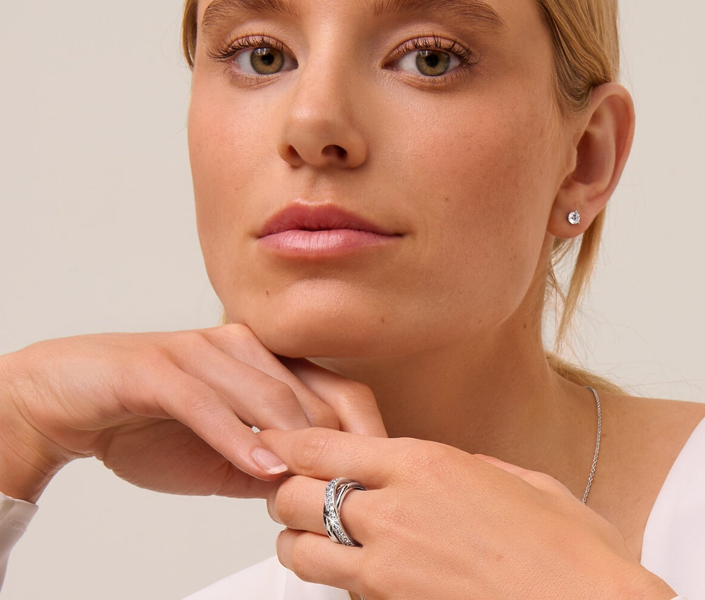 Femme blonde portant des clous d’oreilles en argent 925 solitaire, une chaîne en argent 925 solitaire et une bague Loops avec cristaux.