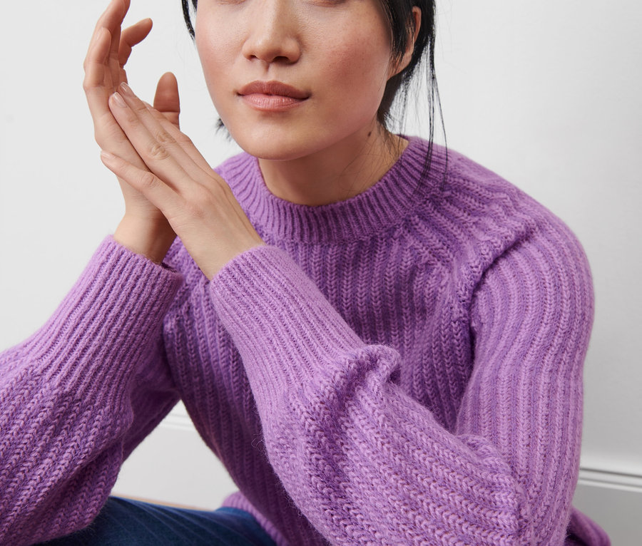 Une femme est assise et porte un pull en maille lilas.