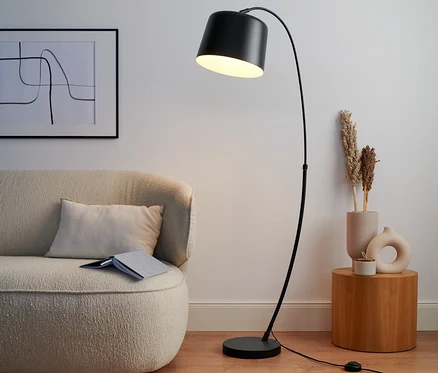 Une lampe recourbée en métal noire est à côté d'un canapé beige.