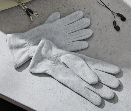 Deux gants en polaire gris sont posés sur une surface grise à côté d'écouteurs et d'un sac.