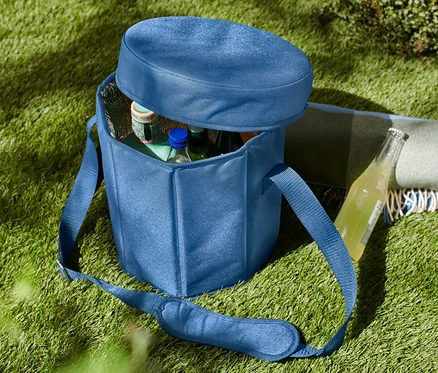 Un sac isotherme bleu 2 en 1 sur l'herbe, partiellement ouvert, avec des bouteilles à l'intérieur.
