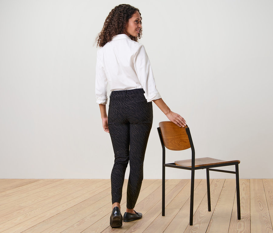 Femme posant en pantalon imprimé en bengaline et chemise blanche à côté d'une chaise.